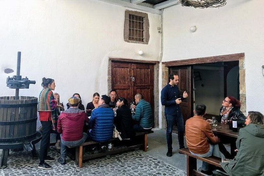 A group of people gathered around a wooden table in an outdoor setting with a rustic building in the background. 3