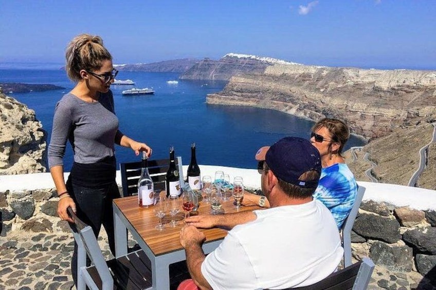 Ett bord med vinflaskor och glas, med utsikt över ett kustlandskap med klippor och havet. 1