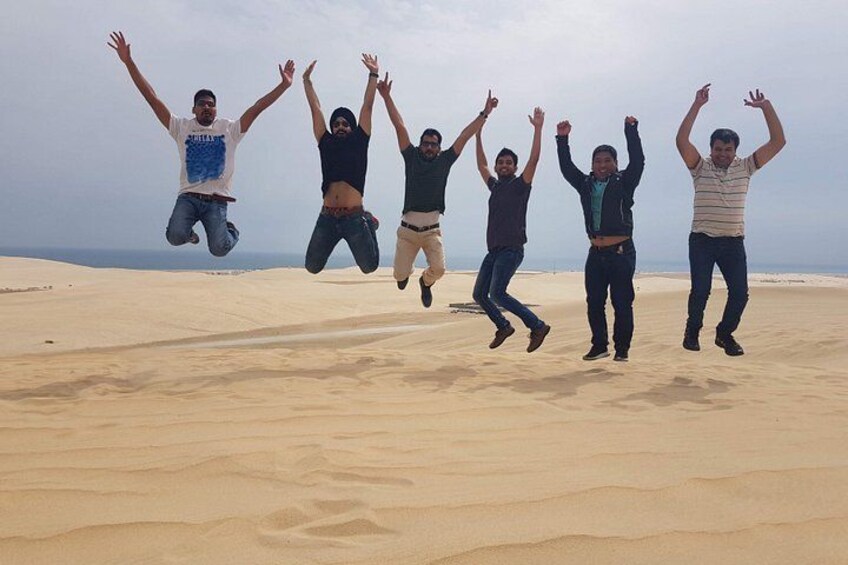 Five people jumping in the air on a sandy beach with the ocean in the background. 3
