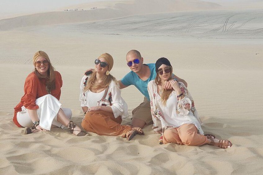 Four people sitting on sand dunes in a desert landscape. 4