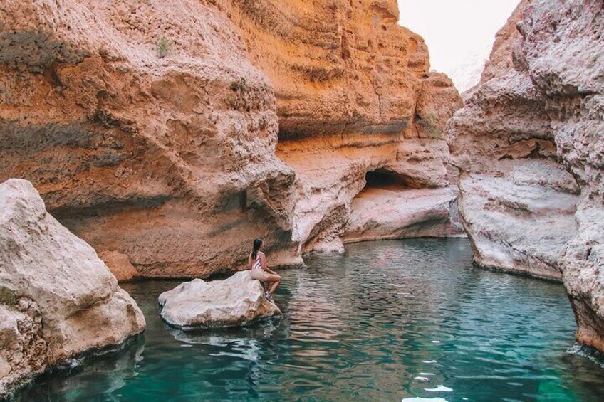A person sitting on a rock by a clear blue pool surrounded by rocky cliffs. 1