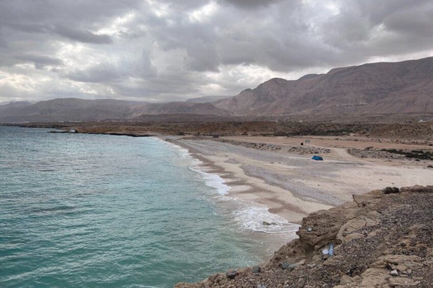 A beach with a rocky shoreline, a clear sky, and distant mountains. 5