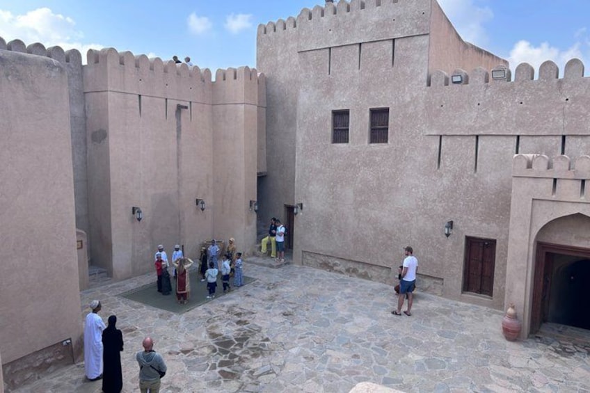 A courtyard with a group of people, a large building with a tower, and a small fountain. 4