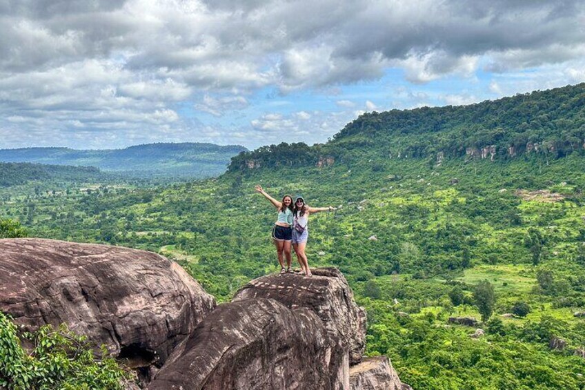 A person standing on a rock with arms outstretched, overlooking a lush green valley. 1