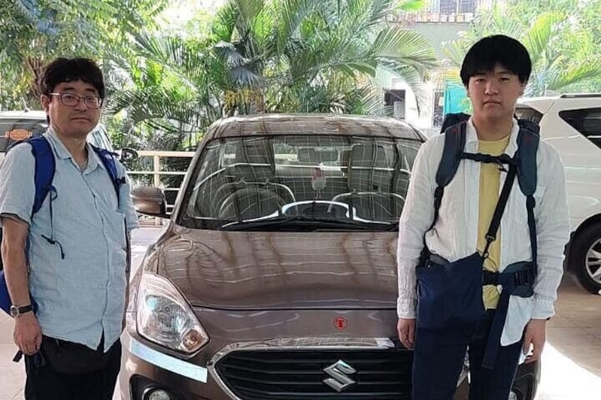 Two people standing in front of a car with a backpack on one person. 2