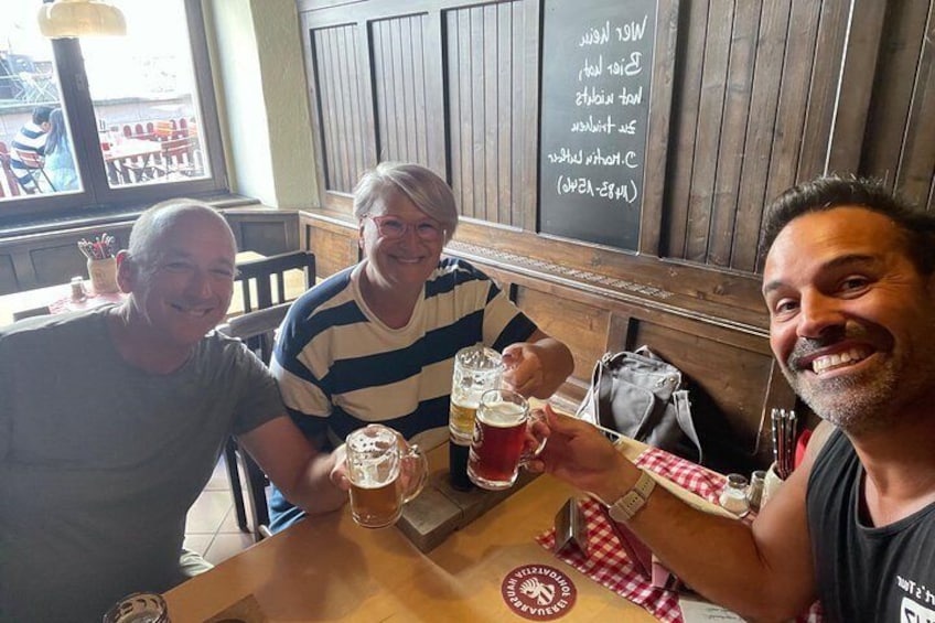 Tres personas brindando con vasos de cerveza en una mesa de madera en un restaurante con menú en una pizarra. 2