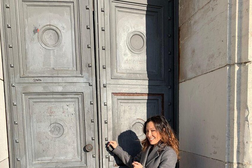 A person standing in front of a large, metallic door with a circular emblem and a handle. 2