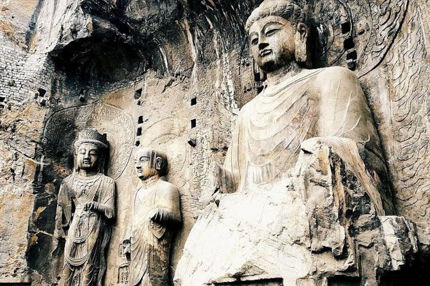 A large Buddha statue with smaller figures in a cave. 5
