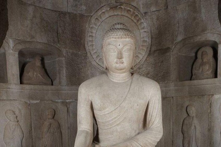 En stent Buddha statue med et skær, omgivet af mindre statuer i alkover. 1