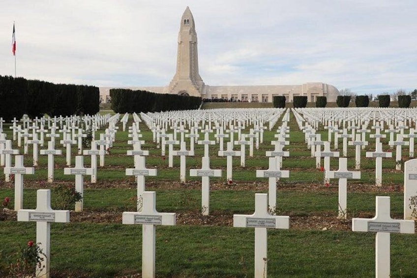 Un cementerio con numerosas cruces blancas, una bandera y un edificio alto al fondo. 1