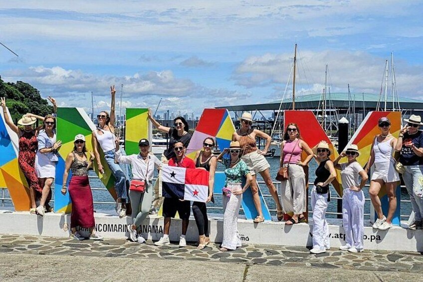 A group of people standing by a waterfront with colorful flags and a city skyline in the background. 2