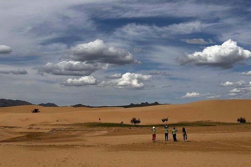 A desert landscape with sand dunes, a few people standing, and a clear sky with clouds. 3