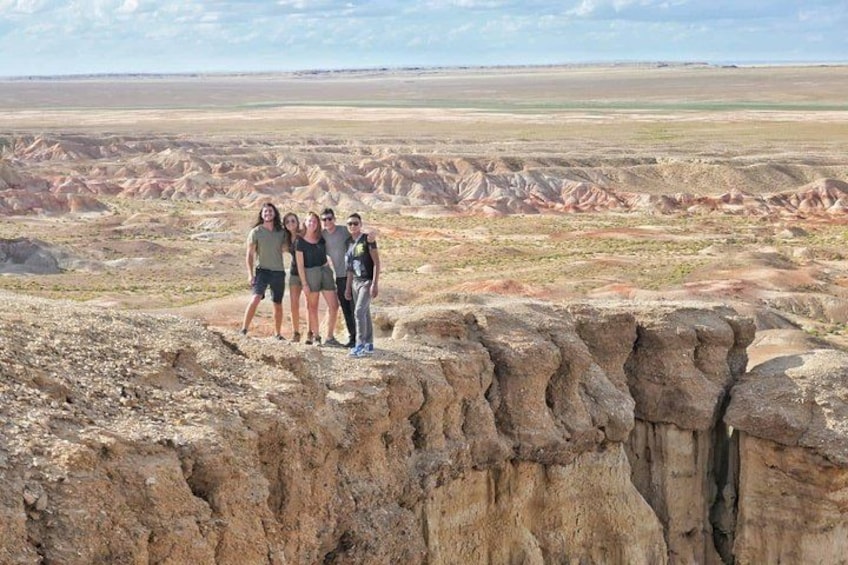 Eine Gruppe von Personen steht auf einem Felsen, im Hintergrund eine weite, zerklüftete Landschaft. 1