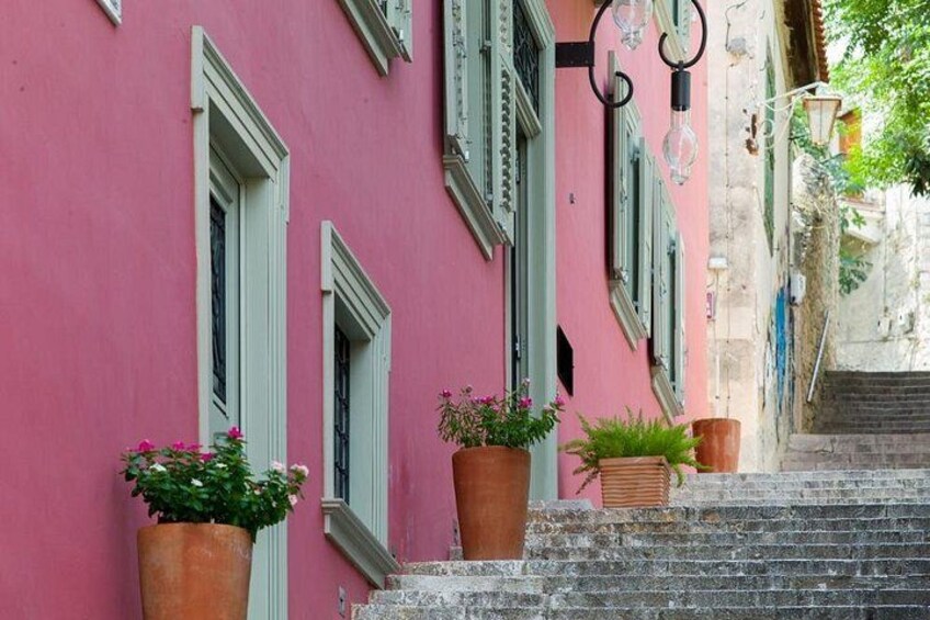 Un bâtiment rose aux volets verts, agrémenté de plantes en pot et doté d’un escalier en pierre. 1