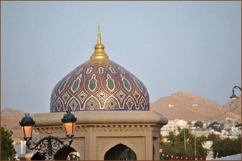 A domed building with intricate patterns, two street lamps, and a mountainous backdrop. 3