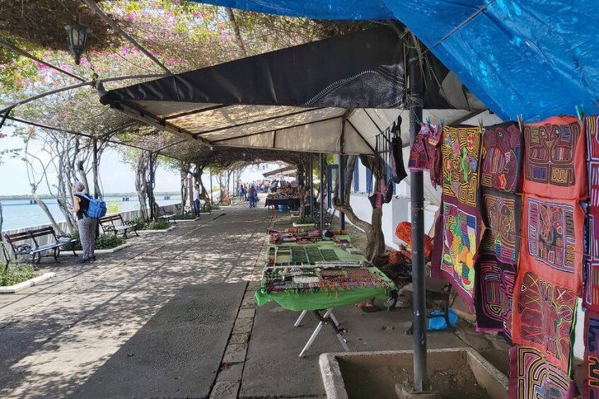 Un étal de marché où sont exposés des textiles aux couleurs vives, et une personne se tient à proximité. 1