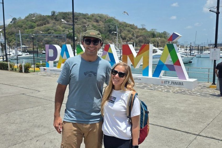Deux personnes se tiennent devant une enseigne colorée sur laquelle on peut lire les lettres « PAM » et « PANAMA », par une journée ensoleillée. 2