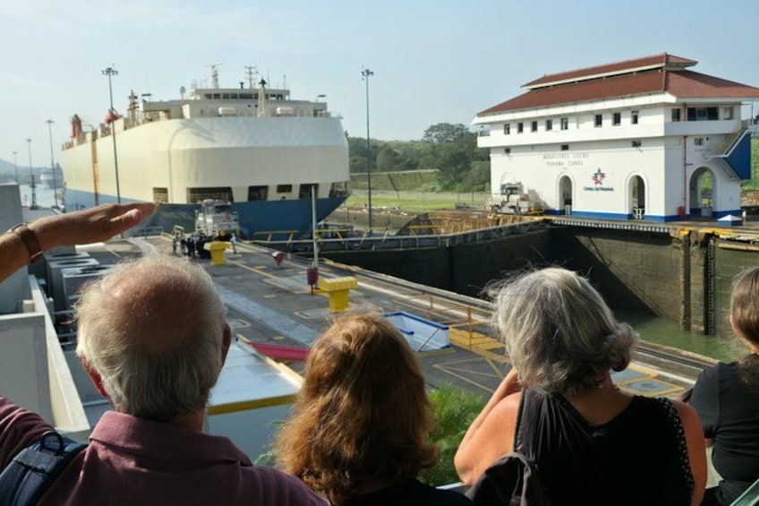 Een groep mensen bekijkt een groot schip dat een sluis passeert. 5