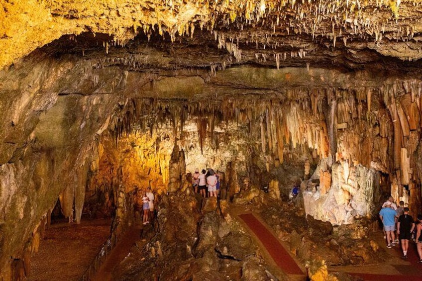 A cave with stalactites and stalagmites, people exploring, and a red path. 2