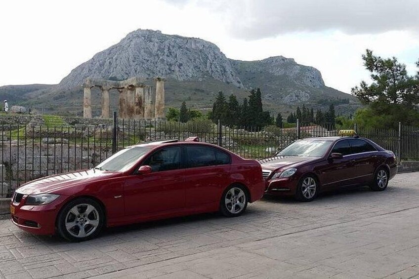 Dos autos estacionados en un estacionamiento con ruinas antiguas y una montaña al fondo. 2