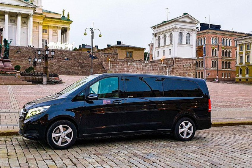 A black minivan parked on a cobblestone street with historic buildings in the background. 1