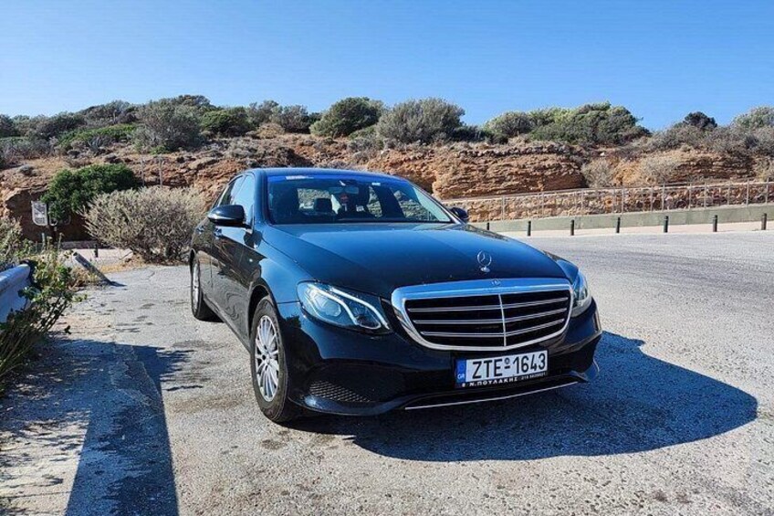 A black Mercedes-Benz parked on a gravel road with a clear blue sky and sparse vegetation in the background. 4