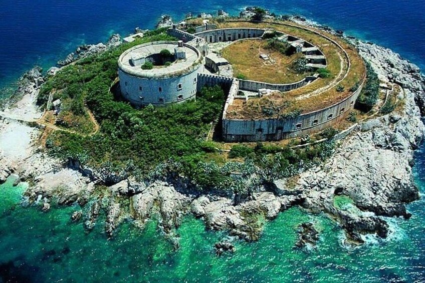 A circular fortress on a rocky island surrounded by clear blue waters. 2