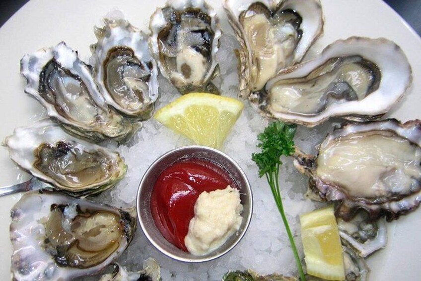 A plate of oysters with lemon wedges and a small bowl of sauce. 1