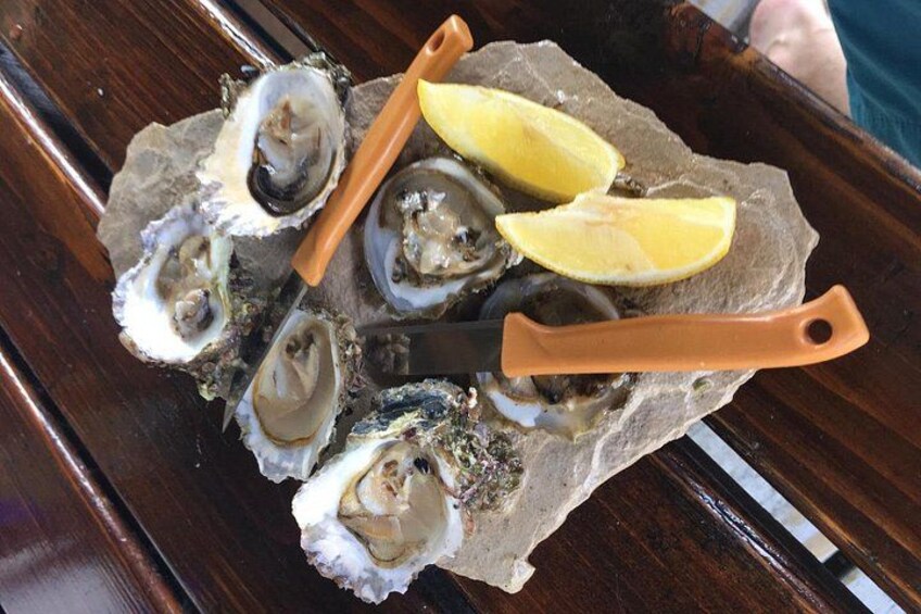 A wooden table with a plate of oysters, lemon wedges, and a knife. 3