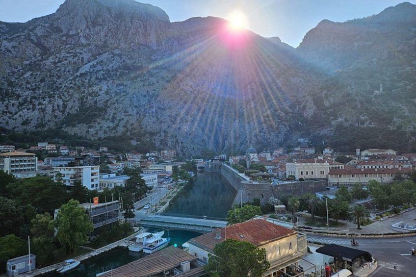 Una cittadina costiera con un'imponente diga sul mare, un porto turistico con imbarcazioni e montagne sullo sfondo. 2