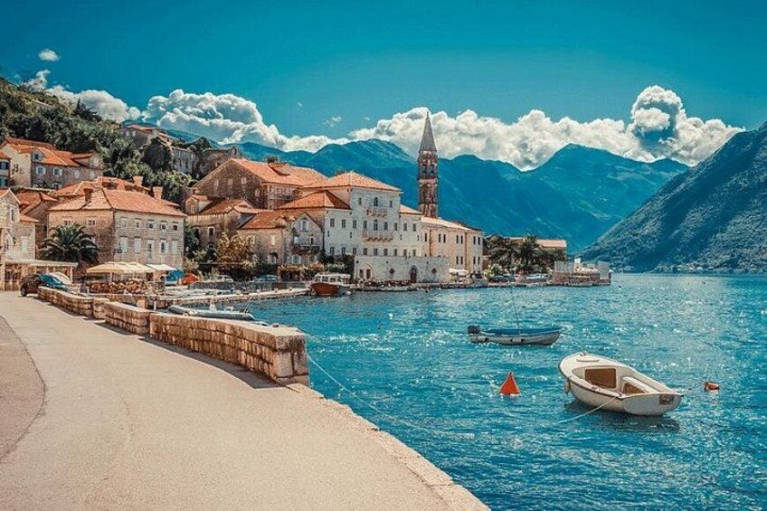 Eine Küstenstadt mit Gebäuden, einer Kirche, Booten auf dem Wasser und Bergen im Hintergrund. 1
