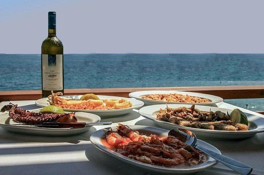 Una mesa con platos de mariscos y una botella de vino, con vista al mar. 2