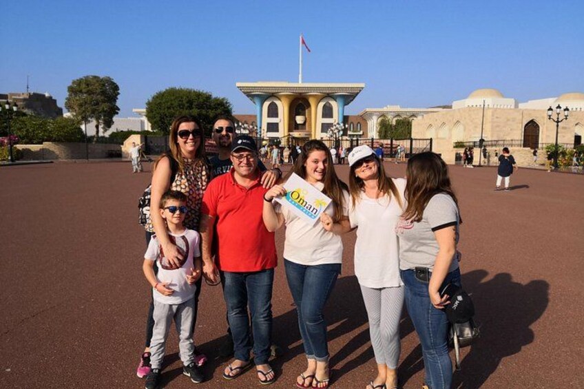 Un groupe de personnes posant devant un bâtiment historique orné d’arches et surmonté d’un drapeau. 1