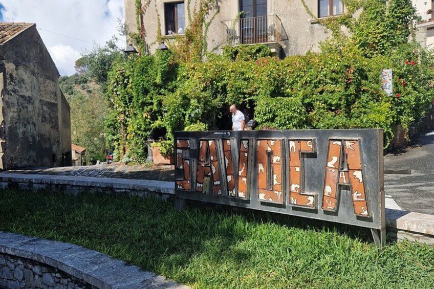 A sign with the word "SANT'IA" surrounded by greenery and buildings. 3