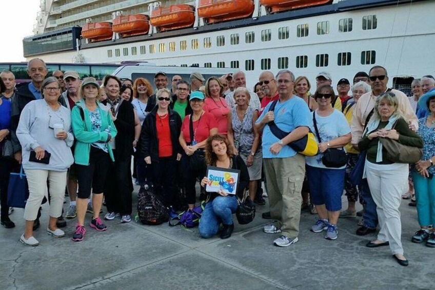 Een groep mensen staat voor een cruiseschip, met reddingsboten zichtbaar op het dek. 2