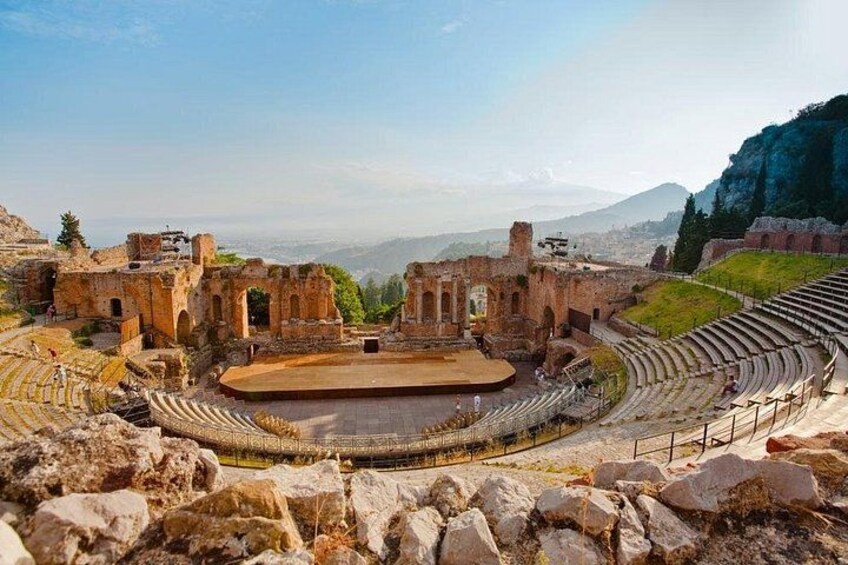 Un antiguo anfiteatro con ruinas y un escenario, rodeado de terreno rocoso y montañas. 1