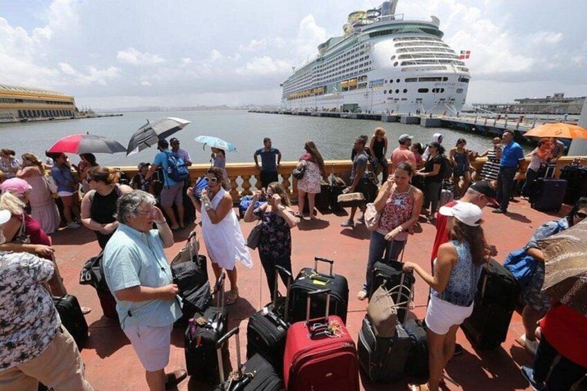 A cruise ship docked at a port with passengers standing on the deck, some with luggage. 2