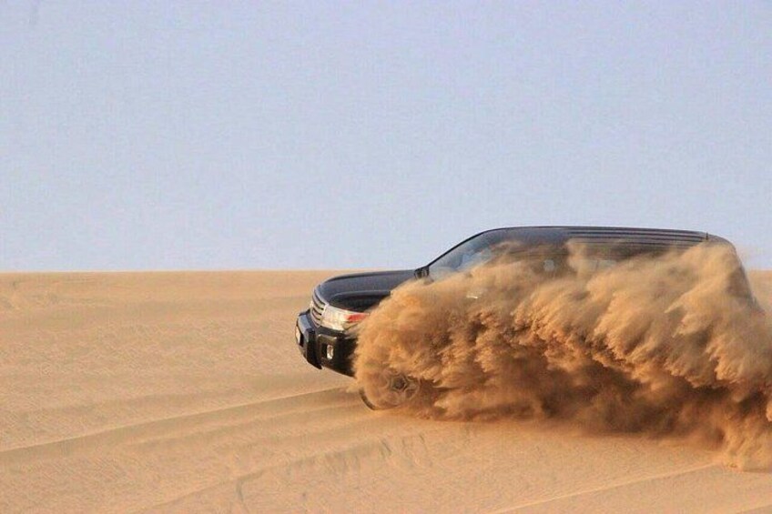 Un veicolo che percorre un deserto, sollevando nuvole di sabbia con gli pneumatici. 2