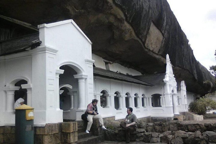 A white building with arches and a large rock formation in the background. 2