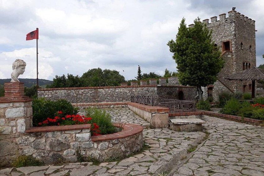 A stone courtyard with a flag, a statue, and a castle-like structure. 1