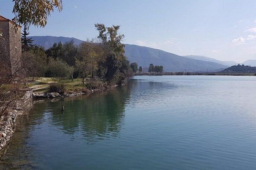 A calm lake with a stone building on the left, surrounded by trees and hills in the background. 3