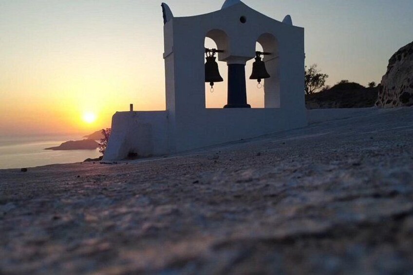 A white bell tower with three bells, set against a sunset over the sea. 4