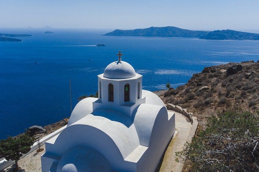 A white church with a dome and cross, overlooking a blue sea and distant islands. 2