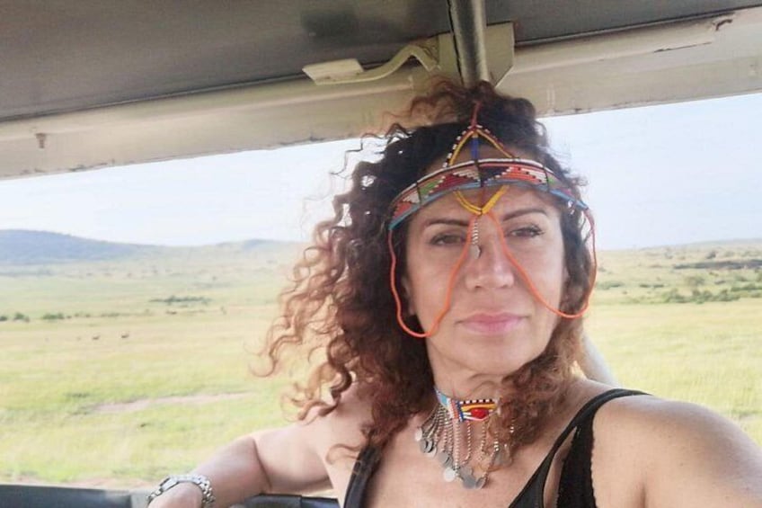 Una persona con cabello rizado, usando una blusa negra y una diadema colorida, sentada dentro de un vehículo con vistas a un paisaje montañoso y con colinas al fondo. 5