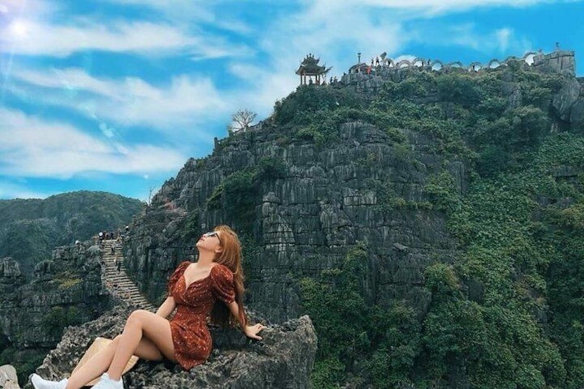 A woman sitting on a rock with a mountainous landscape and traditional architecture in the background. 5