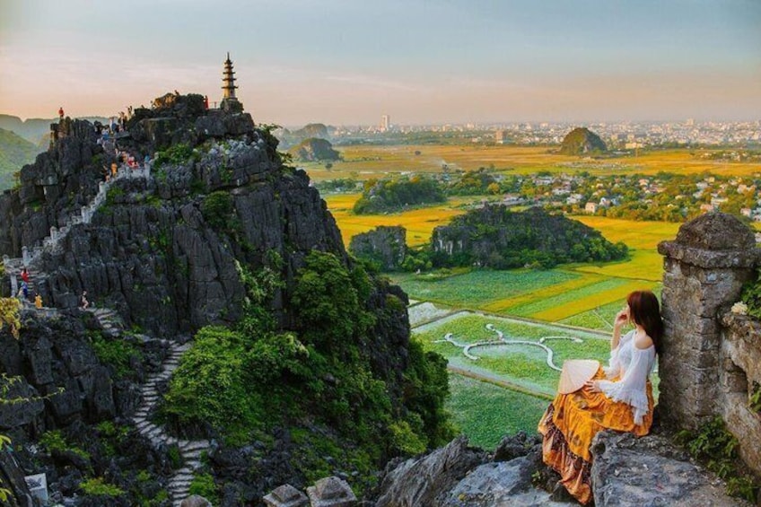 A person sitting on a cliff overlooking a valley with a temple on top. 1