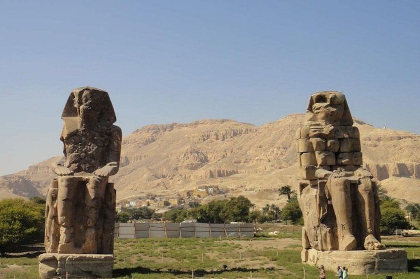 Two ancient Egyptian statues in a desert landscape with mountains in the background. 2
