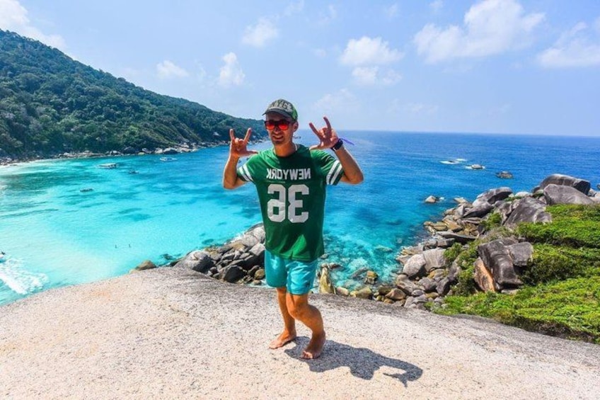 A person standing on a rocky path by a turquoise sea with a mountainous backdrop. 4