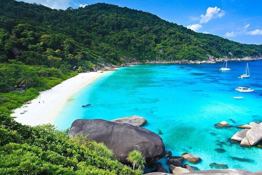 A turquoise beach with white sand, clear water, and sailboats. 2