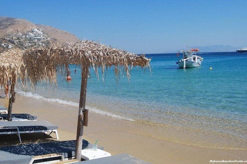 Una spiaggia con un ombrellone di paglia, una barca e montagne sullo sfondo. 2